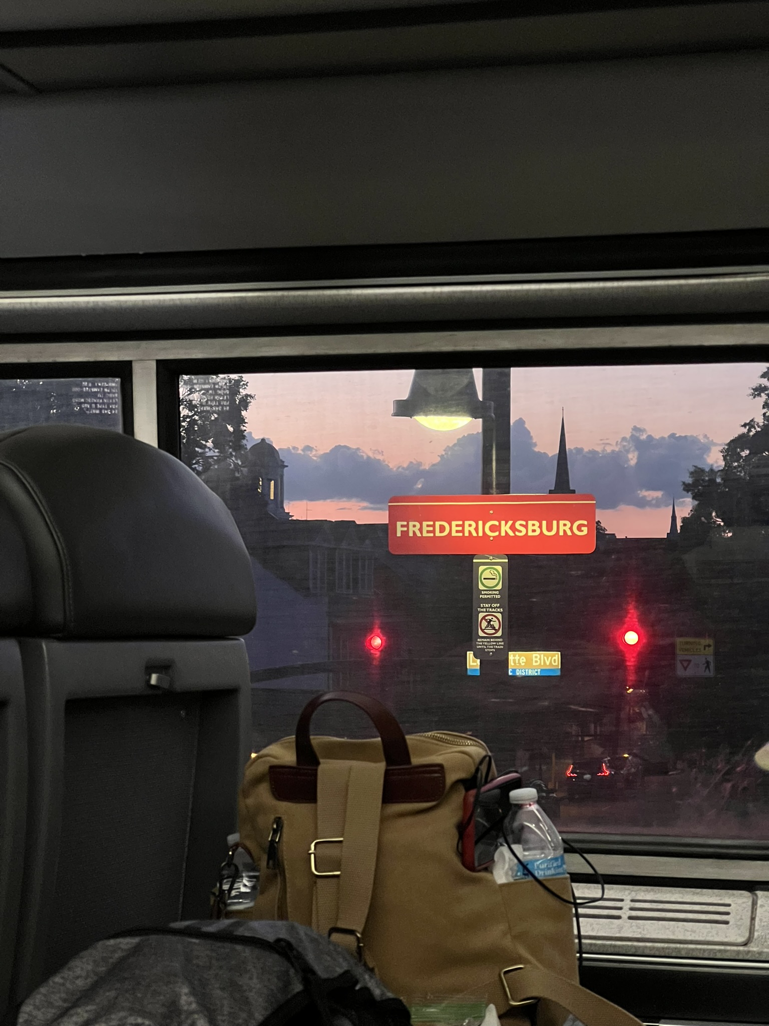 View of Fredericksburg station sign through Amtrak coach window at sunset with luggage in foreground
